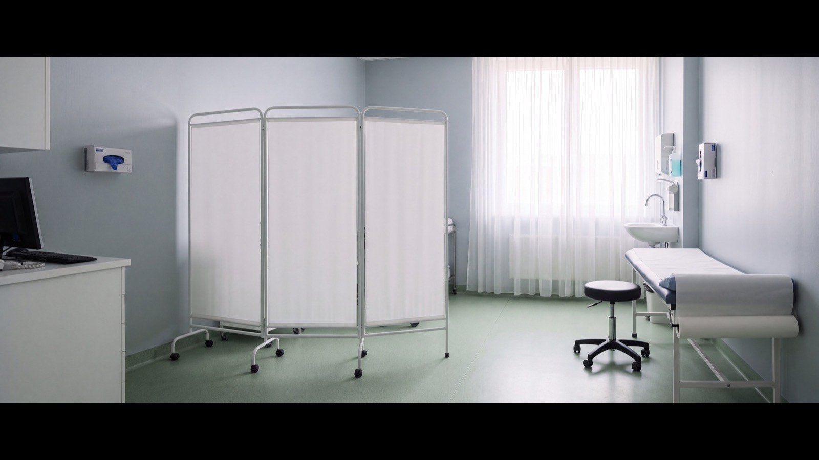 Consultório médico com maca coberta e ambiente reservado para consulta e exame proctológico