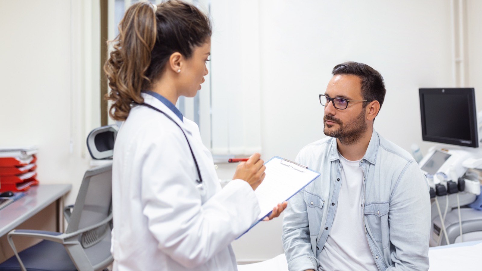 Homem conversa com a médica no consultório enquanto ela anota as informações da avaliação